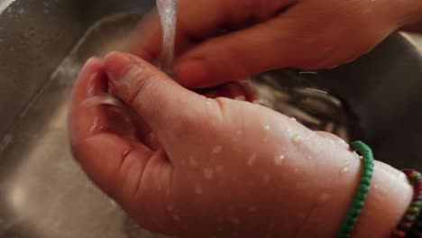 Hands-of-housewife-washing-small-sardine-fish-on-sink-faucet-and-cleaning-to-be-ready-for-cooking,-Mediterranean-diet