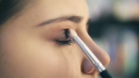 close up view of professional makeup artist hands using makeup brush to apply eye shadows. pro visagiste puts light brown shadows