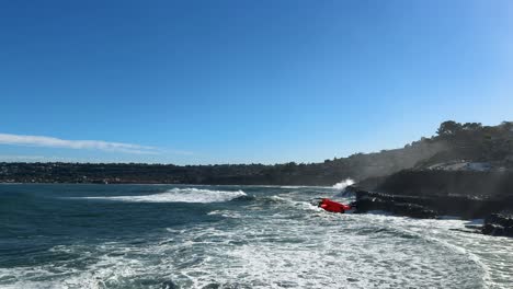 4K-footage-of-drone-flying-from-right-to-left-into-and-out-of-shot-with-large-ocean-waves-crashing-on-cliffs-during-high-tide-in-La-Jolla-Cove,-San-Diego-California