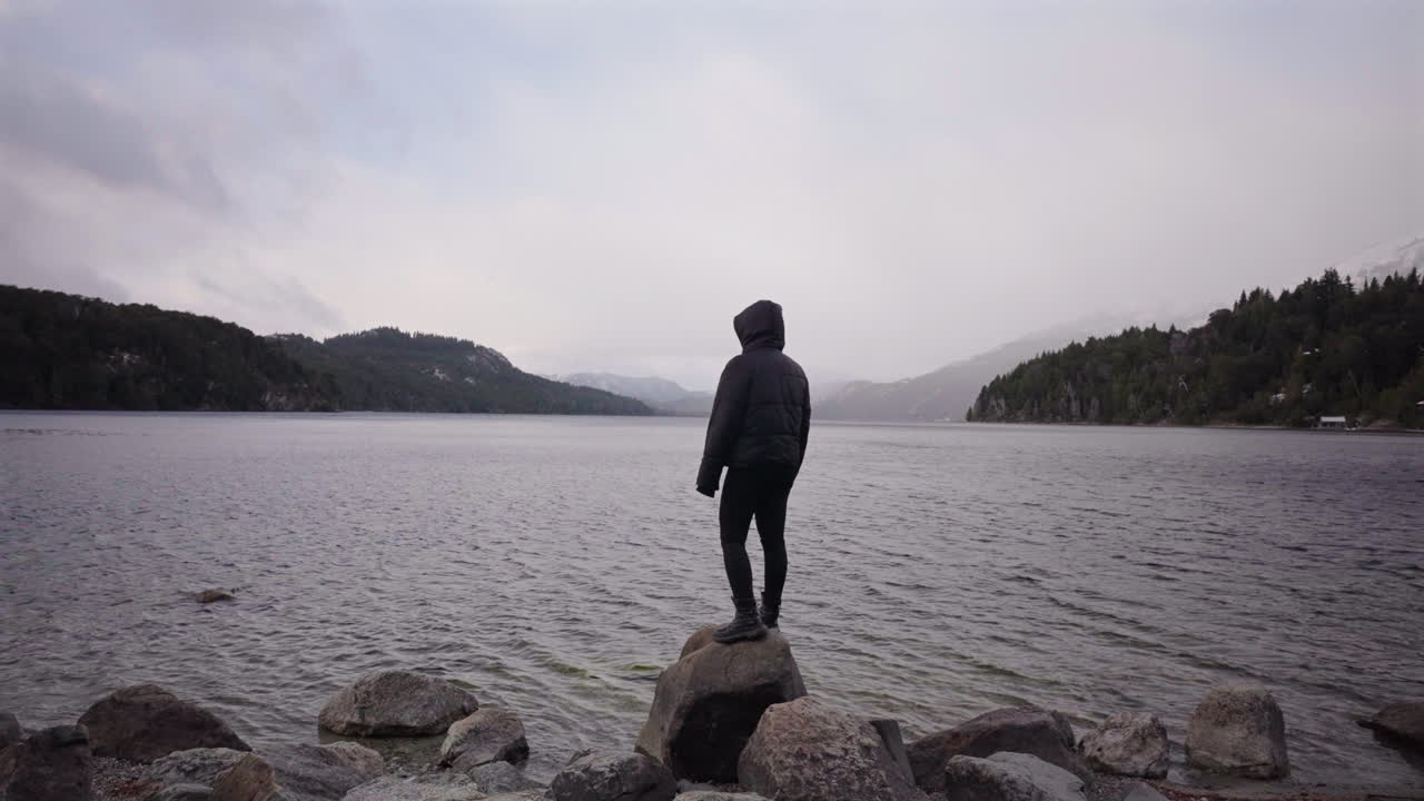 Donna sta in piedi da sola sulle rocce di fronte alle acque nebbiose del lago, quiete, guarigione, introspezione.