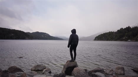woman stands alone on rocks facing the misty waters of lake, stillness, healing, introspection