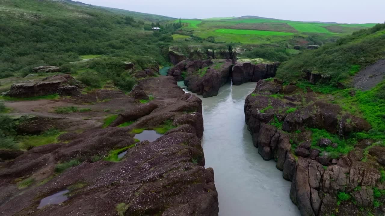 4K-droneopptak fra luften av en bred elv som flyter mellom høye canyonvegger på Island, som avslører dramatisk skala, robuste klipper og mektig naturgeologi