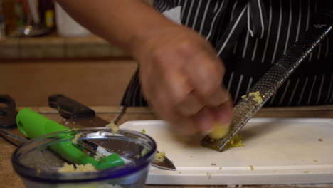 Woman-in-striped-apron-mincing-fresh,-raw-piece-of-ginger-with-grater