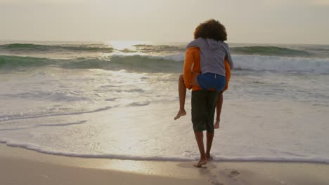 rear view of man giving piggyback ride to woman on the beach 4k