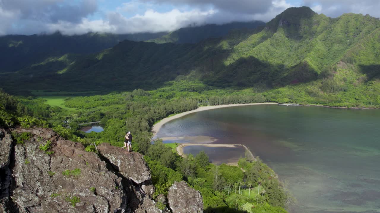 pareja loca coqueteando de pie en la cima de un acantilado peligroso en una caminata de leones agazapados con una vista panorámica excepcional del valle y la bahía de kahana, hawaii