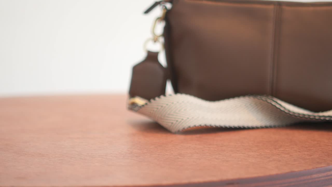 갈색 가죽 어깨 가방이 나무 테이블 위에 놓여 있습니다.