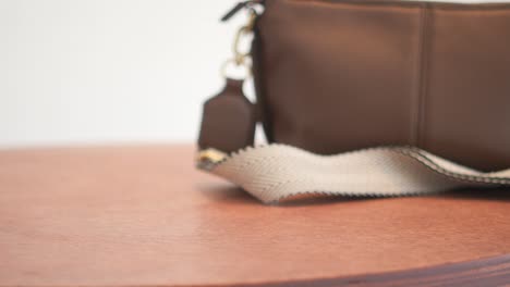 a brown leather shoulder bag is placed on a wooden table.