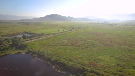 Aerial-view-of-a-beautiful-countryside-field-during-the-sunrise-passing-over-a-lake