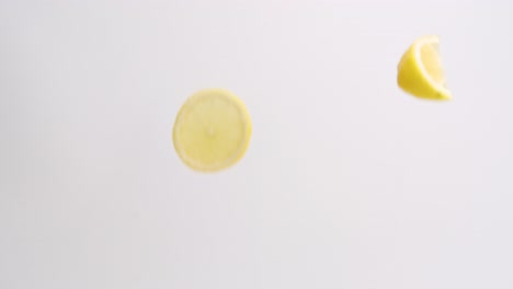 Slices-and-wedges-of-bright-yellow-lemons-raining-on-white-backdrop-in-slow-motion