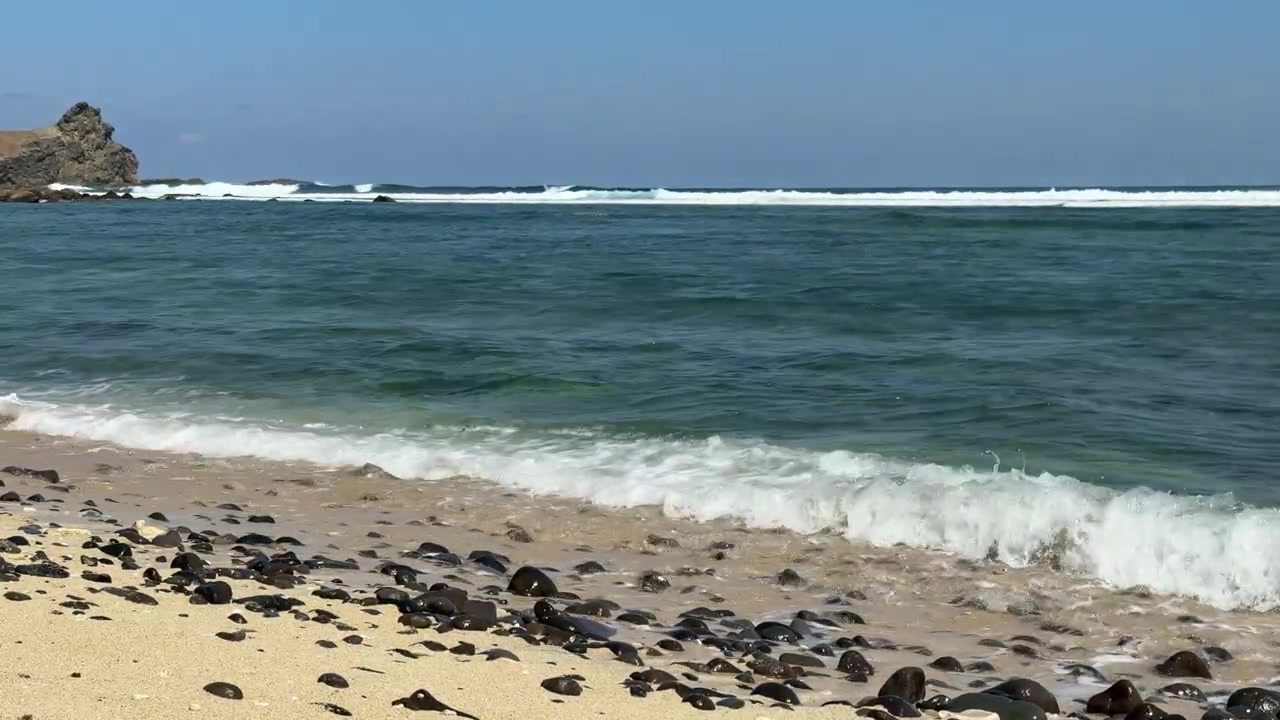 Ondas suaves do oceano quebrando suavemente em uma praia de areia com seixos