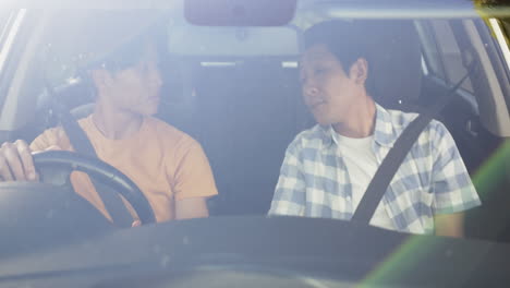 asian father teaching son to drive, pointing and giving instructions in car