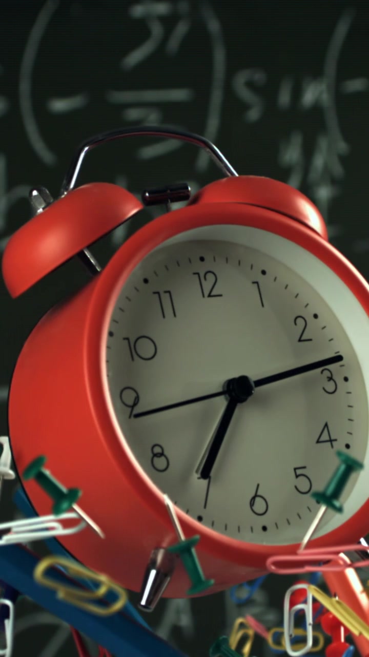 Red Alarm Clock with Office Supplies Against Math Blackboard