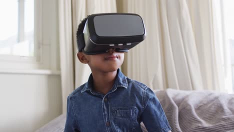 african american boy sitting at home on sofa playing wearing virtual reality glasses