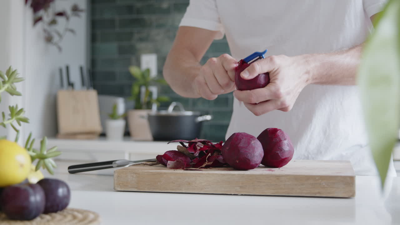 Bidikan Jarak Menengah Seorang Pria Mengupas Buah Bit Segar dengan Pengupas di Dapur Modern