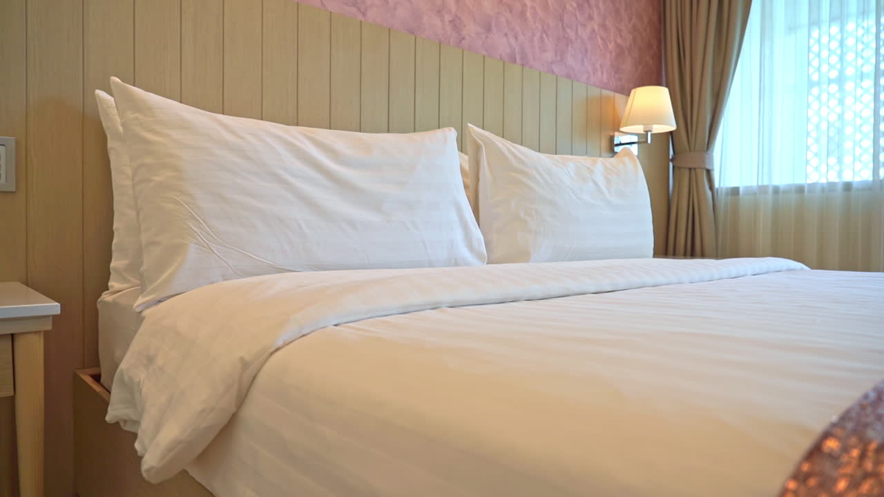 Slow pan of bedroom with bedside table, white sheet, wooden headboard