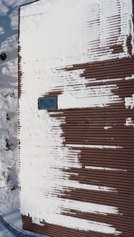 flying above a roof covered in snow. snow melting on a roof in a sunny winter day. vertical aerial drone view of a brown house roof.