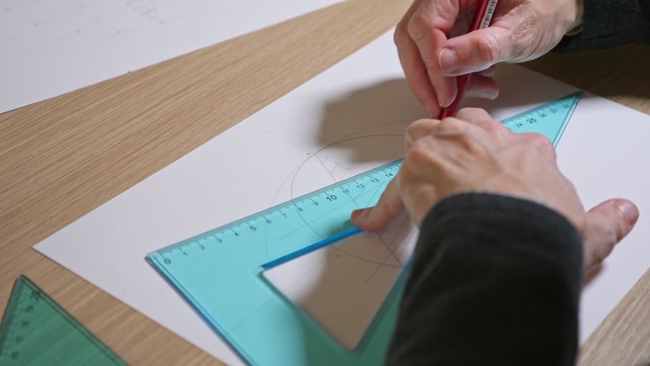 mano femenina haciendo un dibujo geométrico en una hoja de papel con un lápiz y un cuadrado establecido