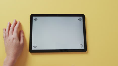 video de las manos de una mujer caucásica y una tableta con pantalla en blanco sobre fondo amarillo