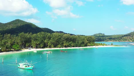 fishing boats floating on calm turquoise lagoon at sunrise on tropical island shore with palm trees hanging over white sandy beach, thailand