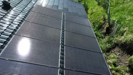 Row-of-solar-panels-on-black,-metal-roof-of-private-home,-aerial-tracking-view