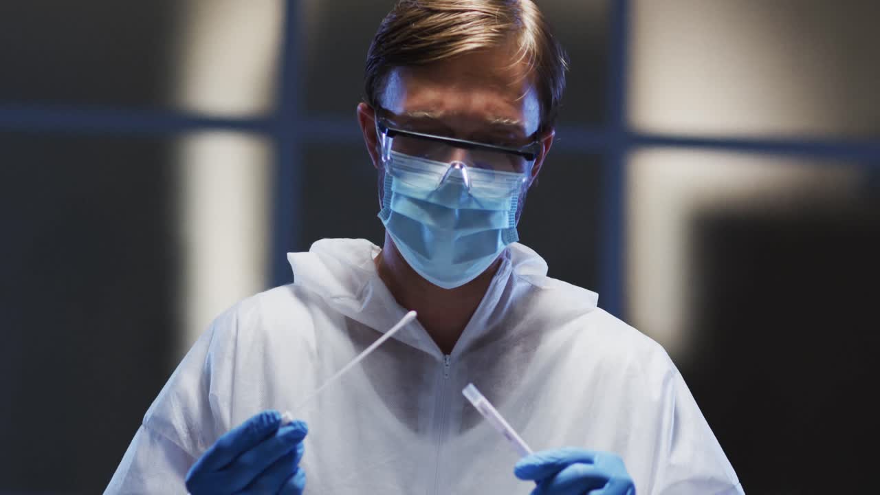Caucasian male medical worker in protective clothing and face mask examining patient swab test