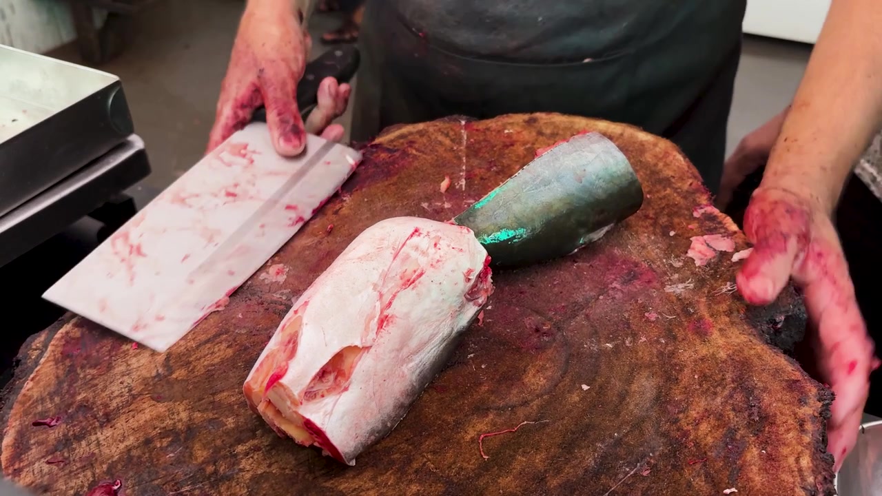 Traditionel fiskehandler hakker frisk fisk med en tung kødøkse på en træblok.