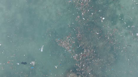 top down ascending drone shot of polluted water filled with plastic trash and dead coral reef in the turqouise tropical water of balangan beach uluwatu bali indonesia