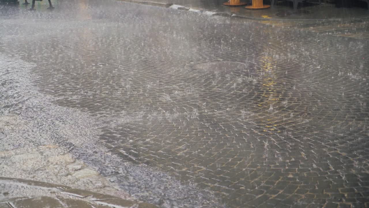 rain drops are falling on the road in the city. Water are flowing by a stream on the wet pavement