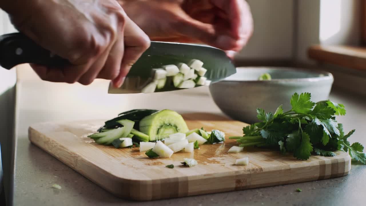 Video verticale: Mani di un cuoco che iniziano a tagliare cetriolo e cipolla con un coltello in cucina, aggiungendo coriandolo.