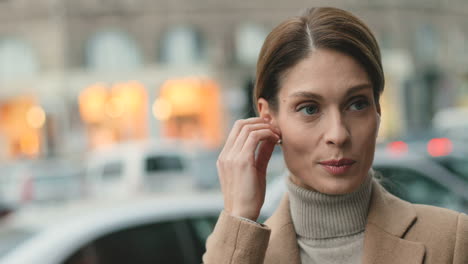 Vista-De-Cerca-De-Una-Mujer-De-Negocios-Caucásica-Usando-Auriculares-Inalámbricos-Mientras-Habla-Por-Teléfono-Y-Bebe-Café-En-La-Calle-En-Otoño