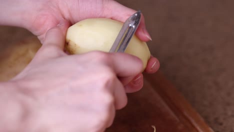 cerrar manos de mujer pelando patatas con pelador de verduras encima de la mesa de la cocina