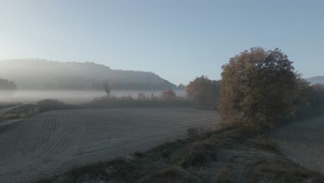 Aerial-drone-fog-landscape-above-dry-agricultural-fields-malla-Barcelona-Spain-Tona,-mountain-background-and-yellow-trees,-in-Spanish-panoramic,-aerial-drone-slow-motion-shot