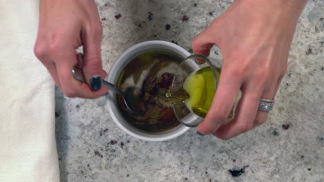 Overhead-view-of-woman-mixing-oil-with-spices-to-create-a-cooking-sauce