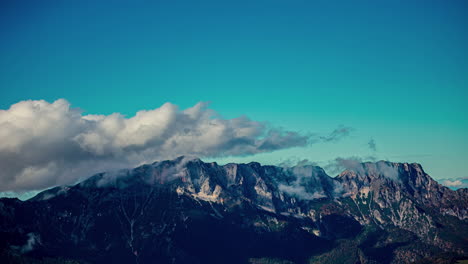 white clouds glide over mountain peaks against a blue sky