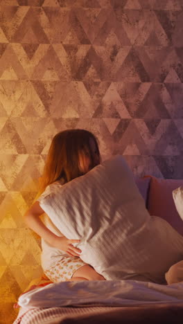 cheerful little daughter and happy mom have funny pillow fight sitting on comfortable bed near play tent with glowing night lamp inside slow motion