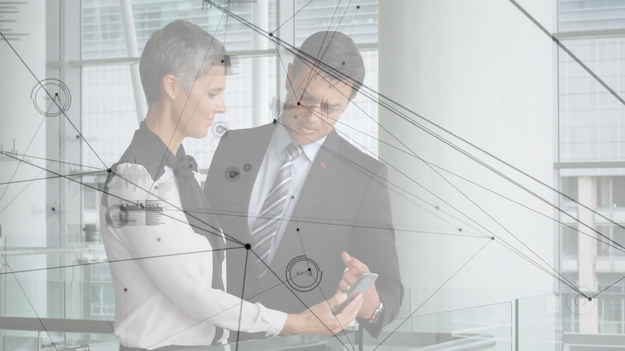 Colleagues holding smartphone and pointing at screen in office, showing technology network charts