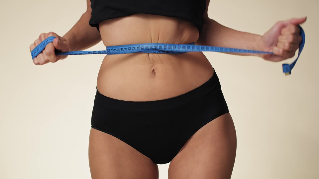 vista frontal de una mujer irreconocible en ropa interior midiendo su cintura con cinta métrica. filmada con una cámara de helio rojo en 8k.