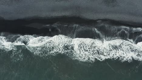 waves rolling onto shore of black sand beach in iceland, aerial