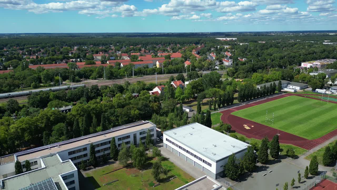 sports facilities at Hennigsdorf high school, including a soccer field, running track and other buildings in residential areas. Smooth aerial view flight fly reverse drone