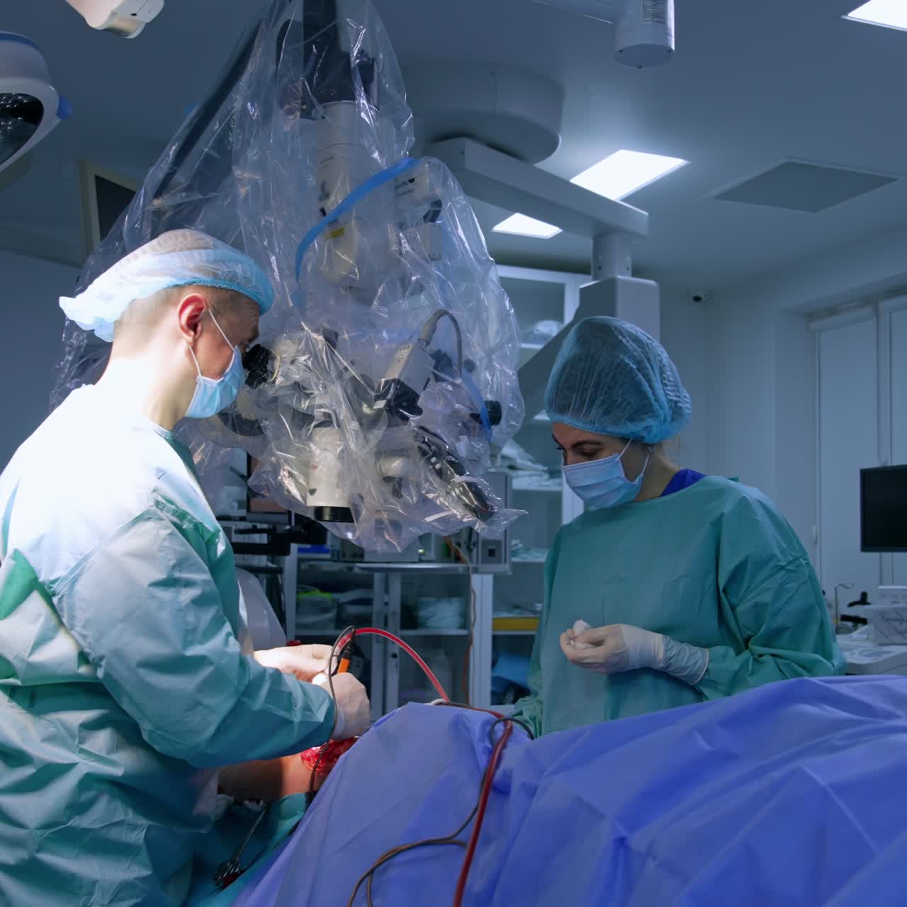 Difficult and delicate operation under microscope. Doctor uses tools looking at the microscope and nurse watches the process