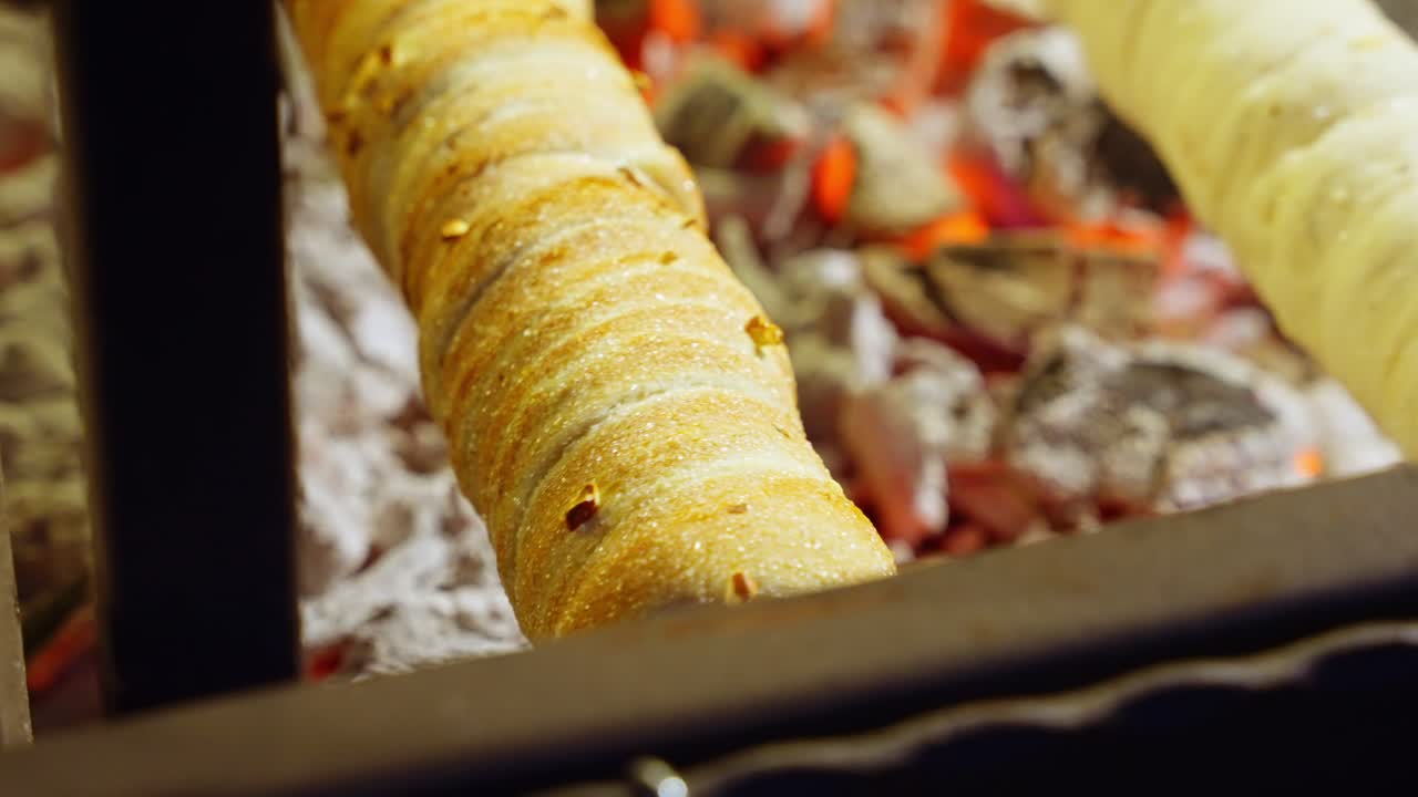 Golden chimney cakes rotating on rollers as crisp crust forms under warm bakery stall lighting