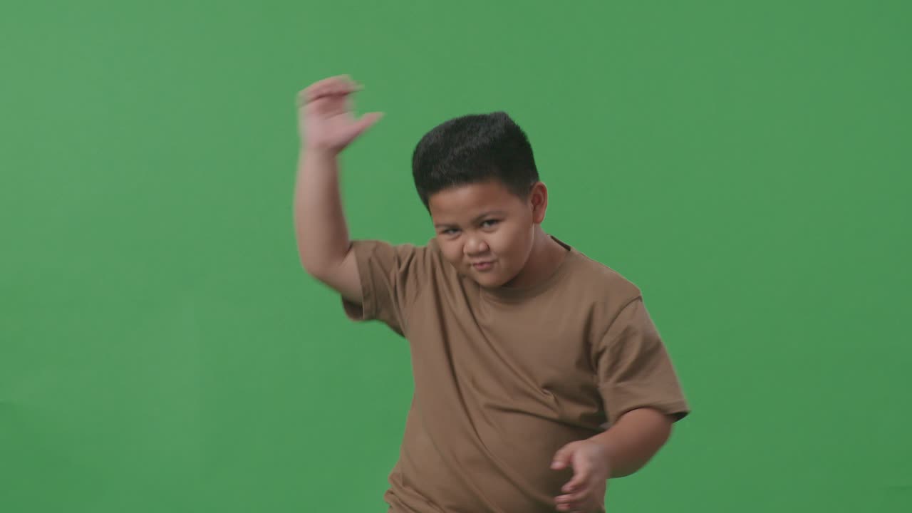 행복한 아시아 소년은 스튜디오에서 녹색 스크린에 서서 축하하고 춤을 추고 있습니다.