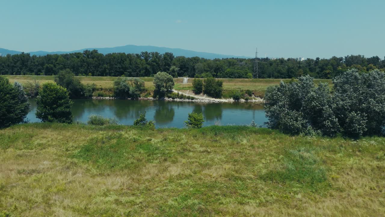 aerial - view of grassy field and trees along the Sava River near Zagreb with mountains behind
