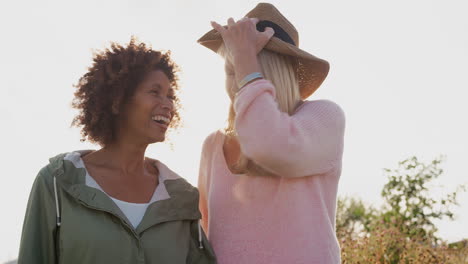 Portrait-Of-Two-Mature-Female-Friends-Smiling-Into-Camera-Against-Flaring-Sun