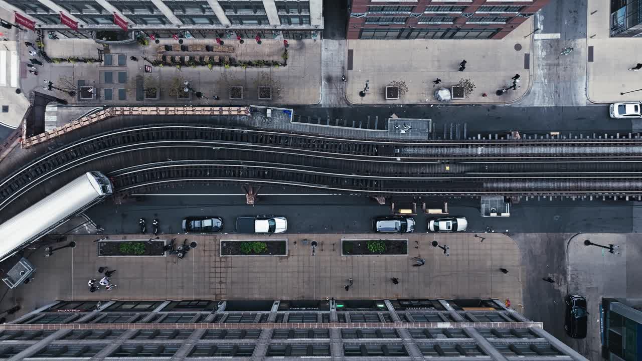 Drone top down descends on public transit tram line arriving at the platform with glistening silver roof