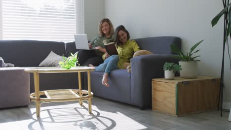 Caucasian-lesbian-couple-using-laptop-and-sitting-on-couch-with-dog