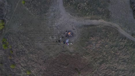 Friends-enjoy-campfire-together-on-clearing-off-path-aerial-top-down-rising