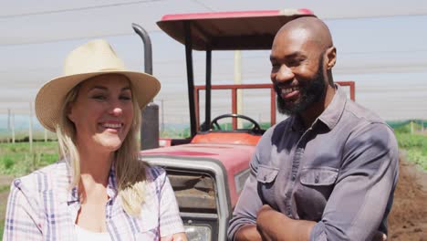 Video-of-happy-diverse-man-and-woman-standing-in-front-of-tractor