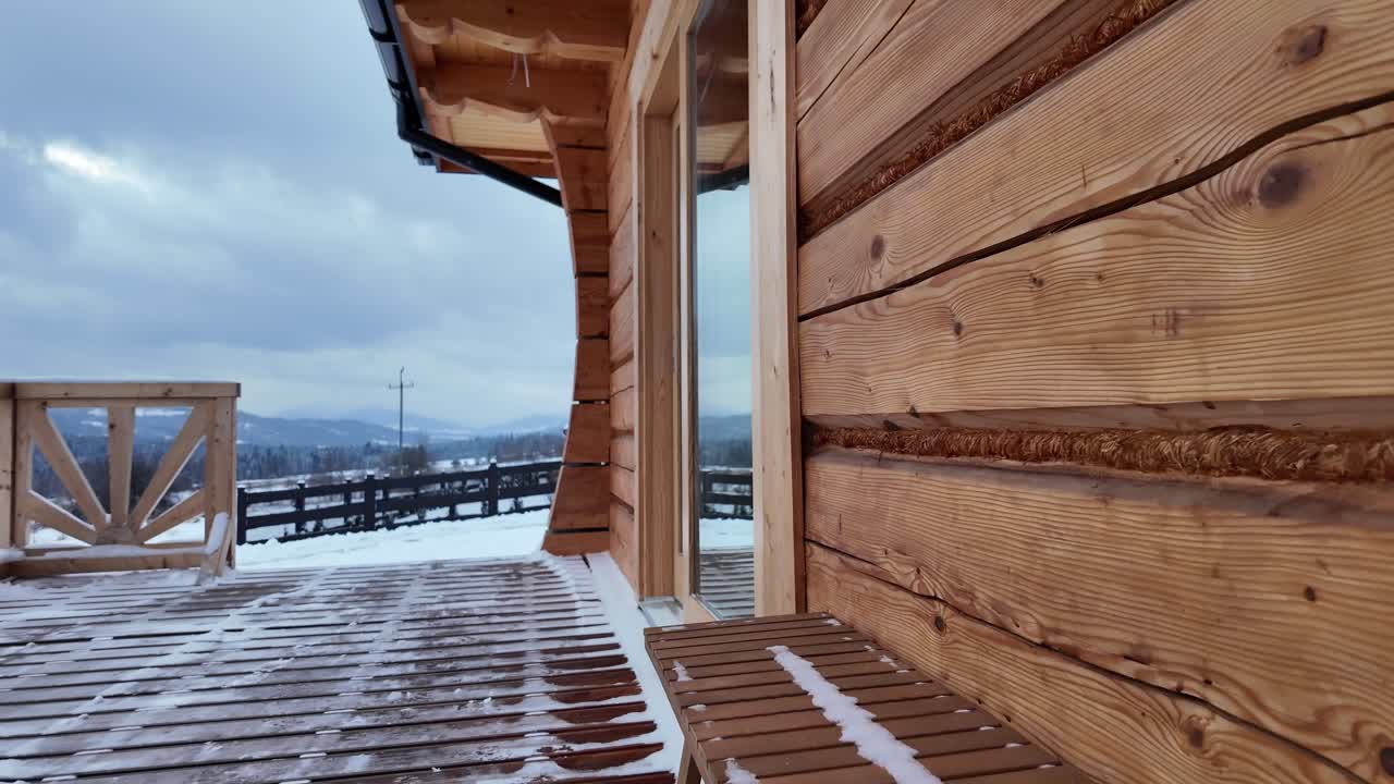 Cloudy sky over a wooden porch and bench of a cozy loghouse, with majestic snowy mountains in the background