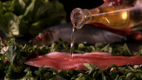 olive oil pouring over fresh trout fillet on a bed of leaves